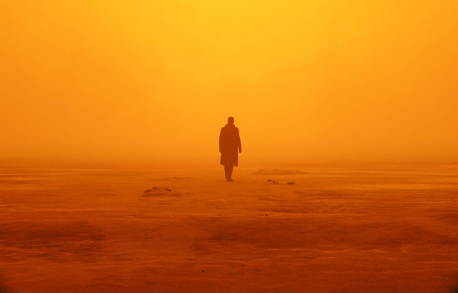 A man in a trench coat looks into the distance in a yellow, dusty environment. The visibility is low so nothing is visible in the distance except yellow sky.